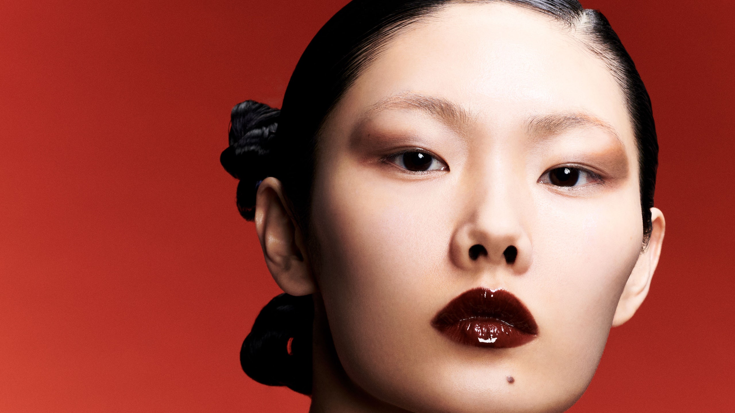 image of woman wearing glossy dark red lipstick while standing in front of red background