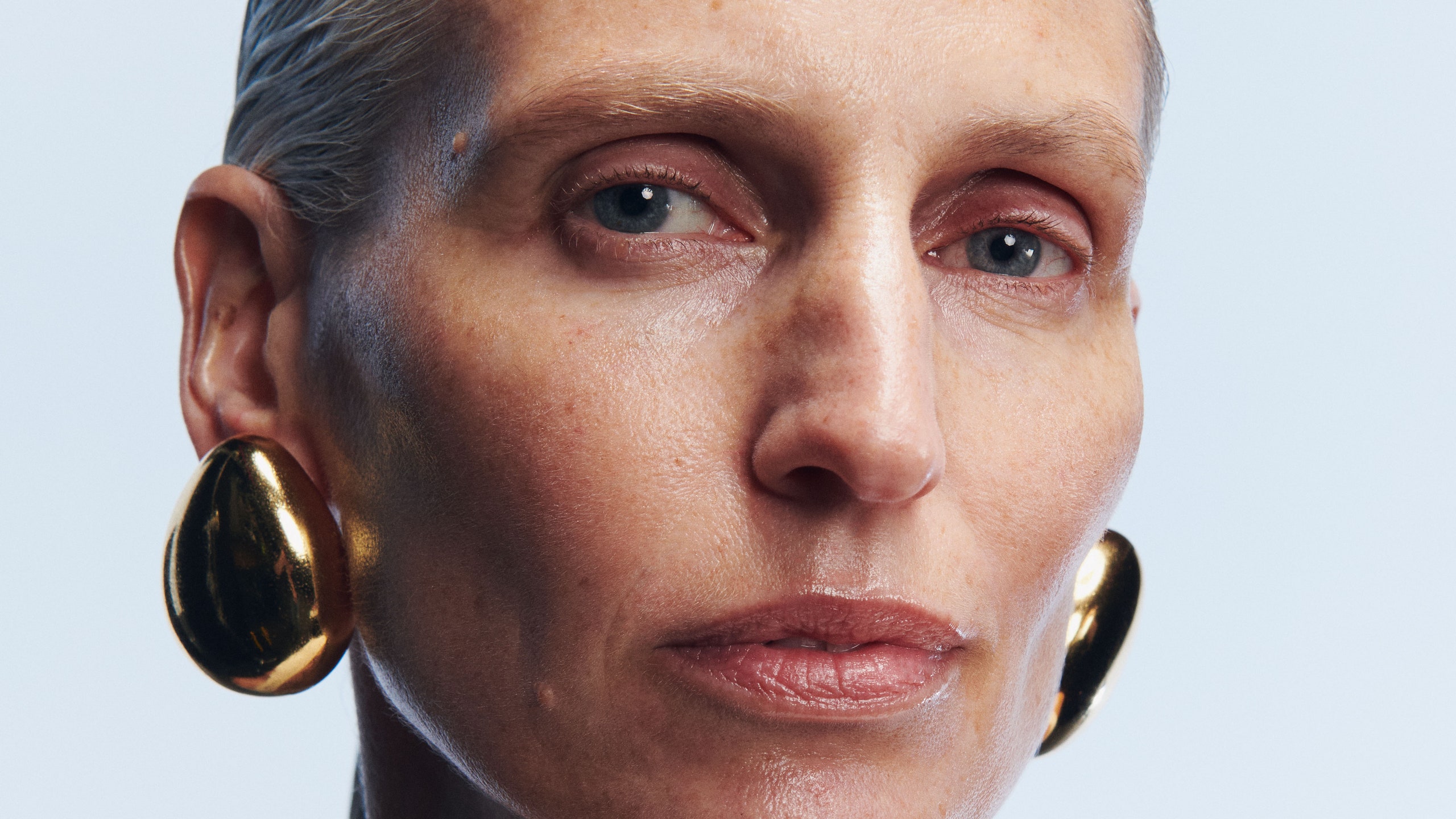 photo of woman with gray hair wearing large gold earrings in front of blue background