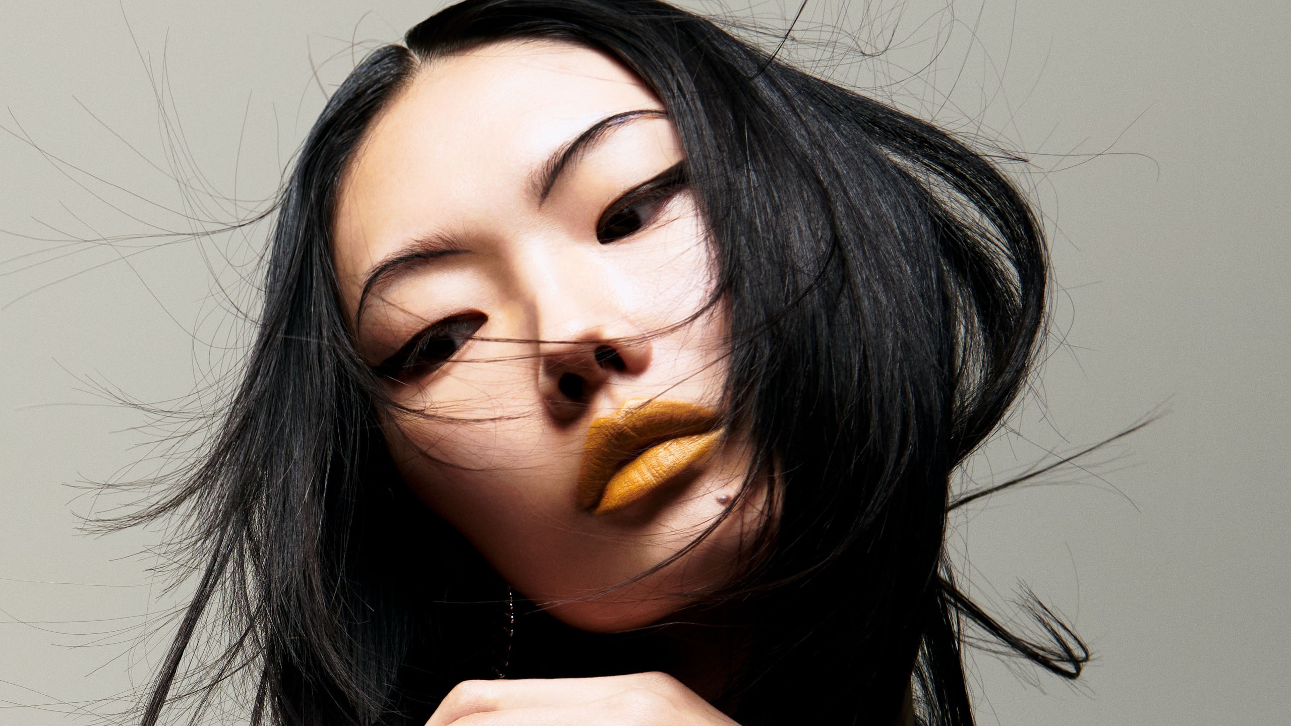 photo of woman with black hair and wearing an orange lipstick in front of gray background