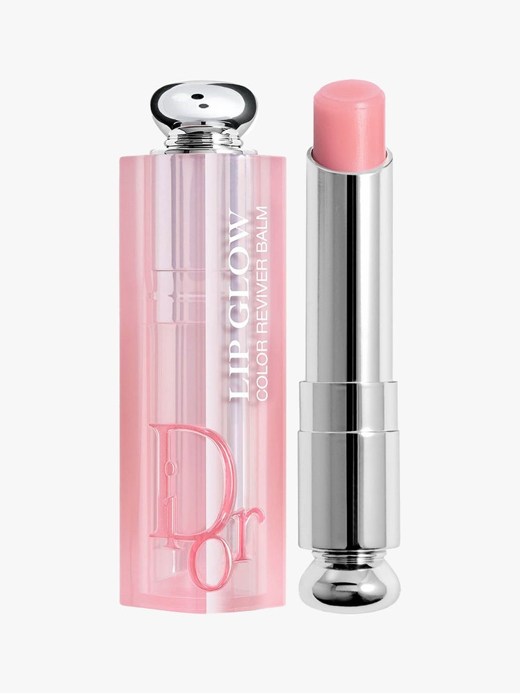 Dior Addict Lip Glow silver twist up tube of lip balm on light gray background with pink cap to the side on light gray...