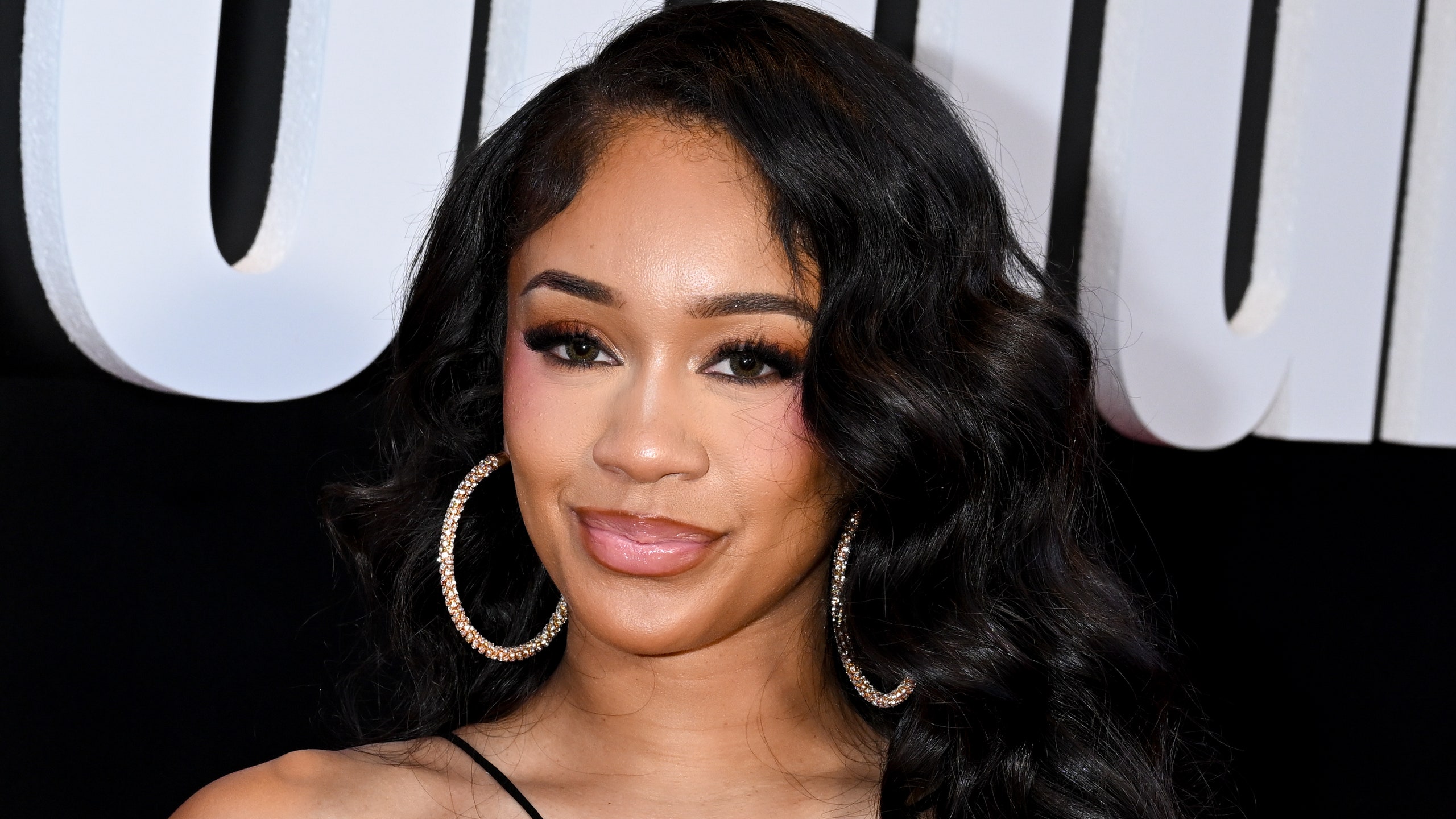 Saweetie poses at an event in a cutout black dress and long curls.